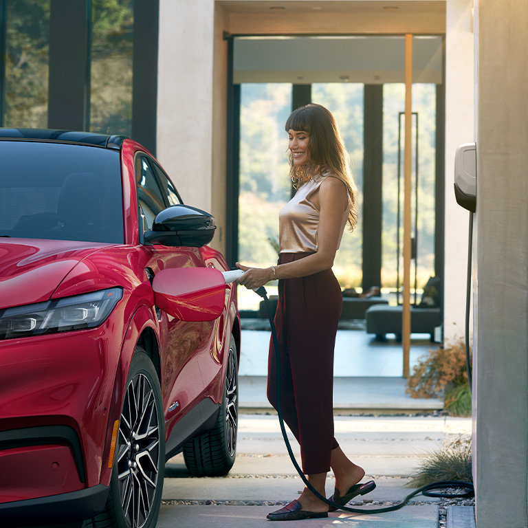 Une femme branche une Mustang Mach-E à une borne de recharge Ford.