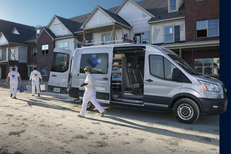 Une fourgonnette commerciale Ford E-Transit stationnée devant une maison.