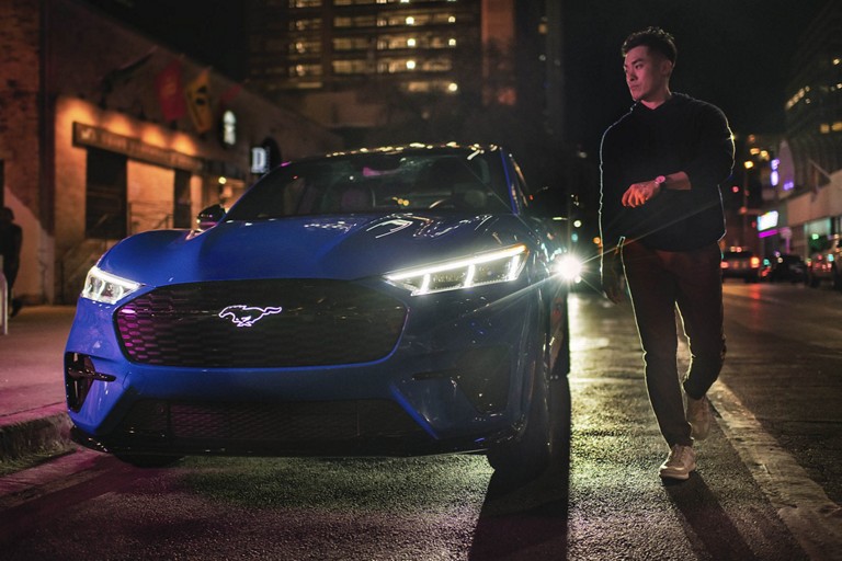 Une personne passe à côté d’une Ford Mustang stationnée en ville de nuit
