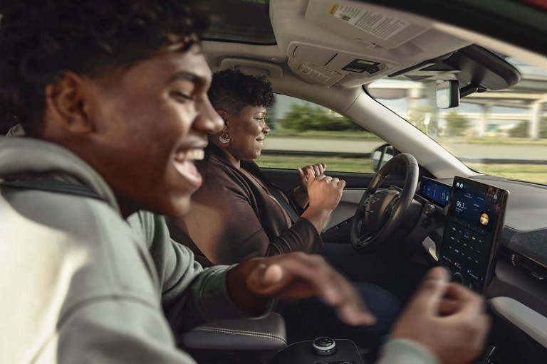 Vue de l’intérieur d’un véhicule dans lequel le conducteur ne tient pas le volant et rit avec son passager