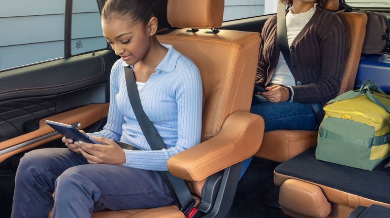 Deux enfants souriants utilisant des appareils mobiles assis dans la deuxième et la troisième rangée d’un VUS Ford.