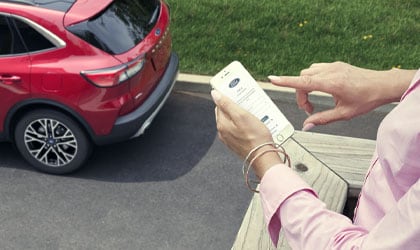 Femme debout sur un balcon tenant un téléphone cellulaire avec un véhicule Ford Escape 2021 en arrière-plan.
