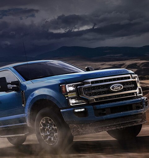 Ford Super Duty 2020 en bleu vélocité conduit sur un chemin de terre avec le soleil en arrière-plan