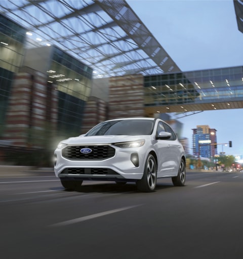 Ford Edge S T 2020 en bleu performance Ford dans un virage sur une route près de collines avec une grande ville en arrière-plan