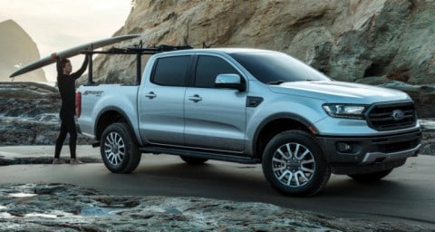 Homme plaçant une planche de surf sur le toit d’un véhicule Ford Ranger LARIAT 2020 stationné sur le sable près d’une plage rocheuse
