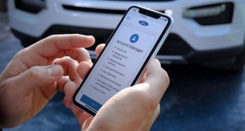 Un homme tient un téléphone montrant la page d’accueil Crédit Ford, debout devant un véhicule Explorer X L 2020