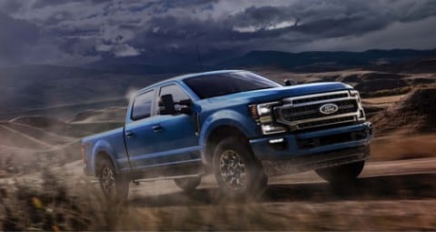 Ford Super Duty 2020 en bleu vélocité conduit sur un chemin de terre avec le soleil en arrière-plan