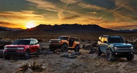 Deux Ford Broncos 2021 et un Ford Bronco Sport 2021 stationnés dans le désert avec une chaîne de montagnes en arrière-plan