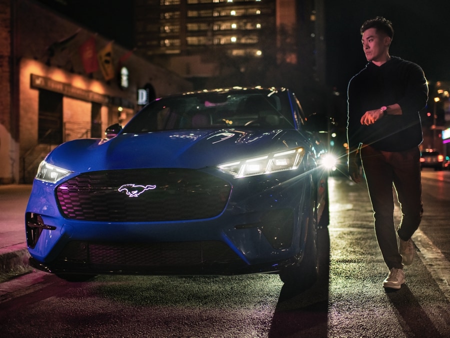 Un homme à l’extérieur d’une Ford Mustang Mach-E bleue la nuit dans la ville.