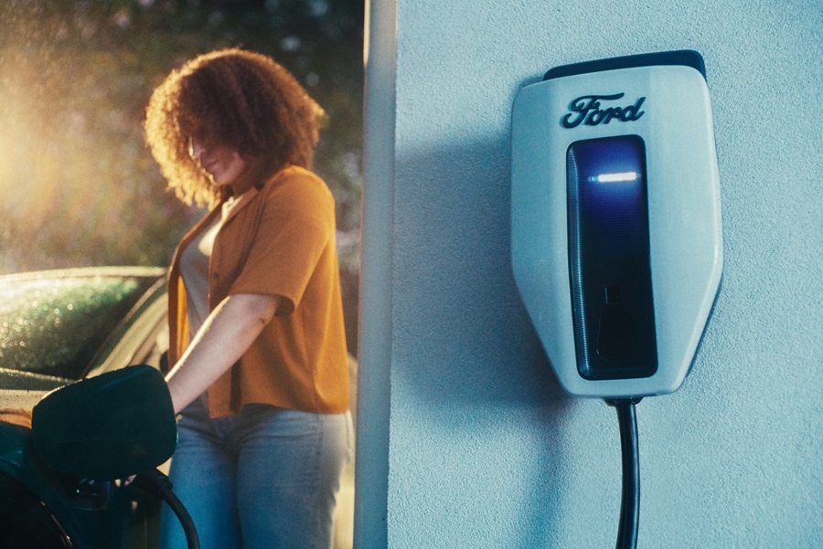 Une femme rechargeant sa Mustang Mach-E dans son garage avec la borne de recharge Pro au premier plan.