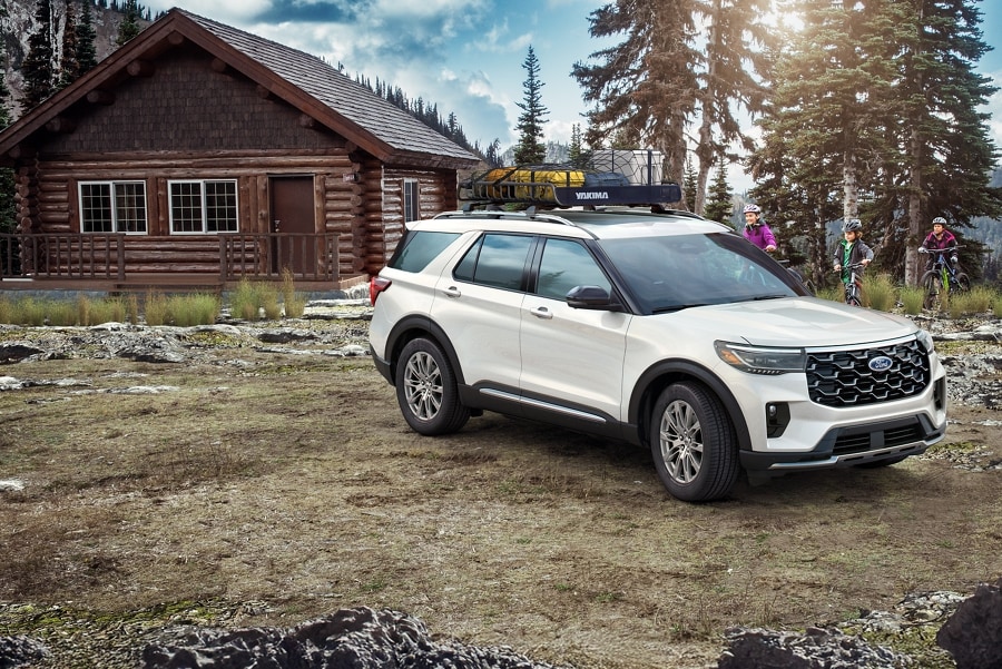 Ford Explorer® 2025 blanc stationné à l’extérieur d’une cabine rustique alors qu’une famille à vélo approche