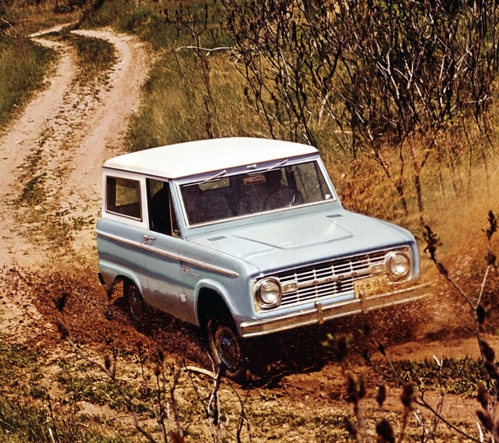 Ford Bronco fourgon Sport 1967 conduit sur un chemin poussiéreux