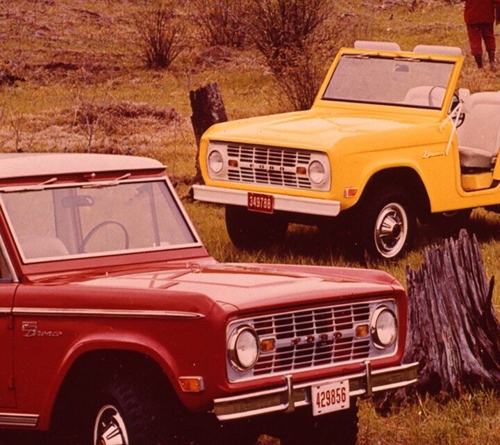 Trois Ford Bronco 1969 stationnés en pleine nature alors qu’un groupe de personnes marchent à proximité