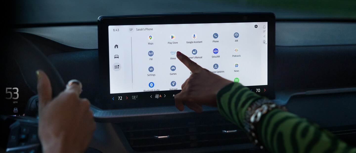 Une personne conduit un véhicule Ford pendant qu’une passagère sélectionne Alexa dans la liste des applications sur l’écran tactile central.