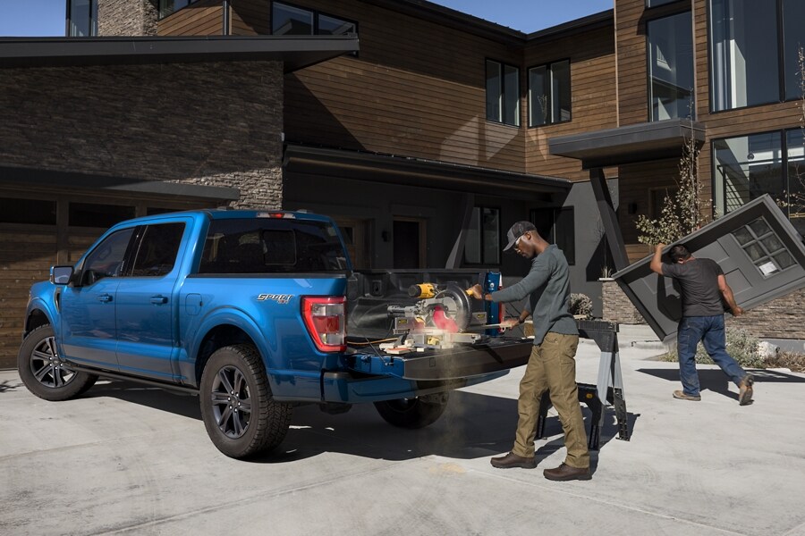 Homme coupant du bois à l’aide d’une scie électrique sur le hayon d’un Ford F-150® LARIAT SuperCrew® 2022 en bleu Atlas devant une maison