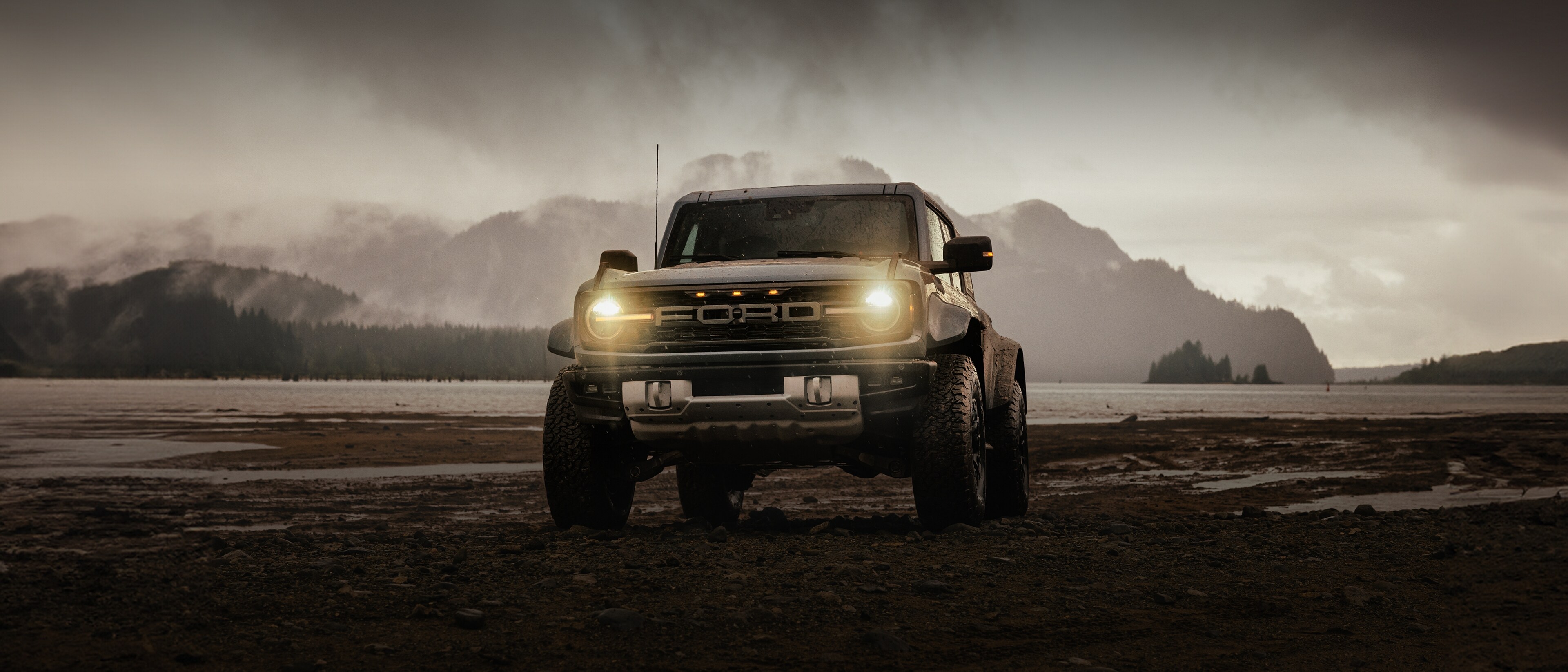 Un VUS Ford Bronco® 2025 sur une vasière près d'une montagne enneigée, avec des nuages de pluie menaçants.