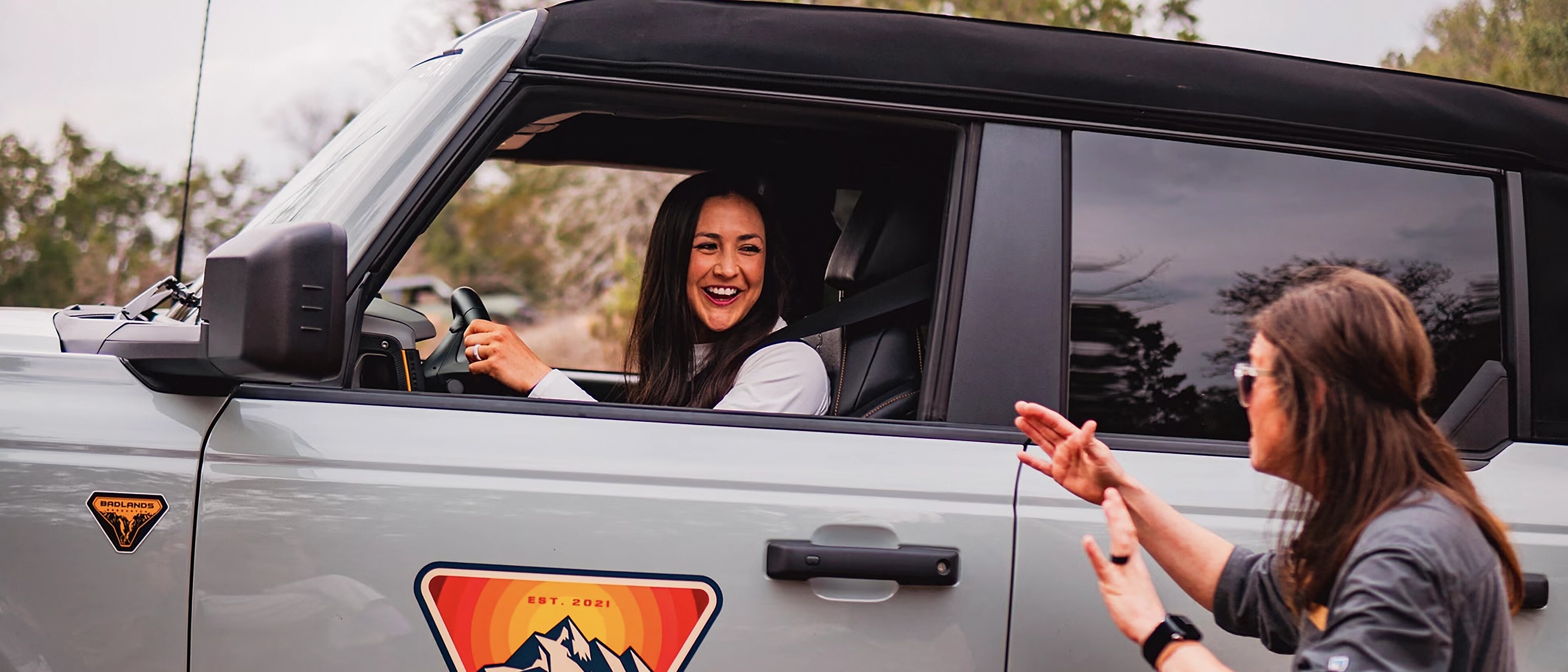 Une femme conduisant un VUS Ford Bronco® 2025 lors d’une expérience Bronco Off-Roadeo®, avec un instructeur donnant des directives de l’extérieur du véhicule