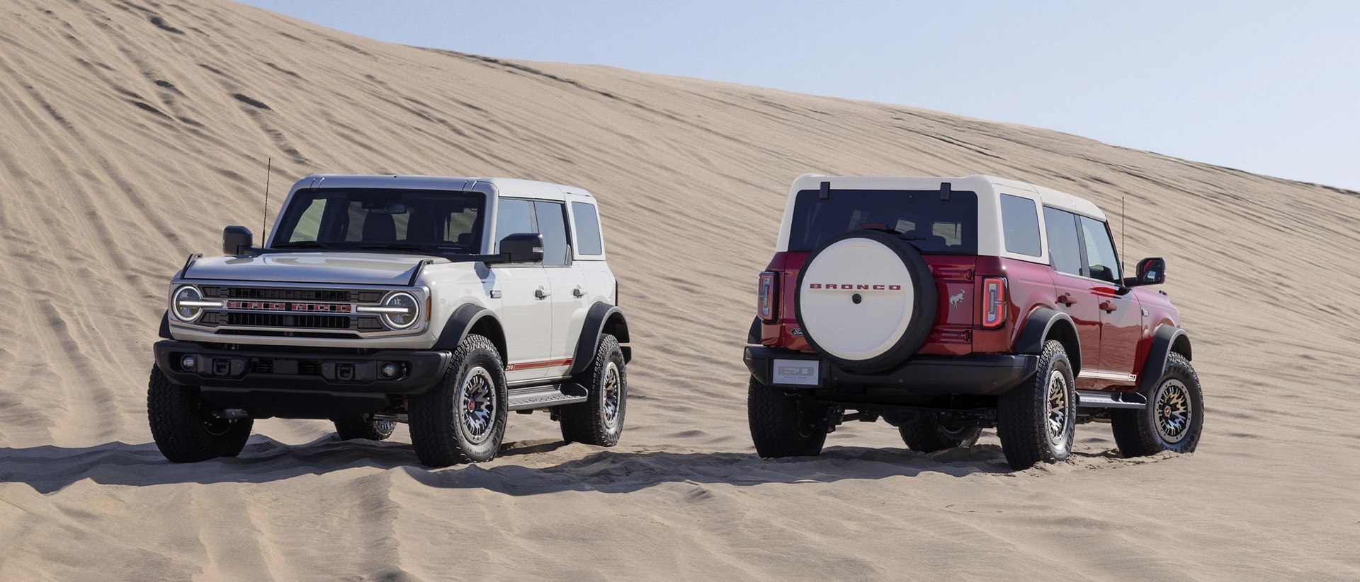 Deux VUS Ford Bronco® 2026 avec l’ensemble 60e anniversaire en option stationnés sur une dune de sable un matin ensoleillé