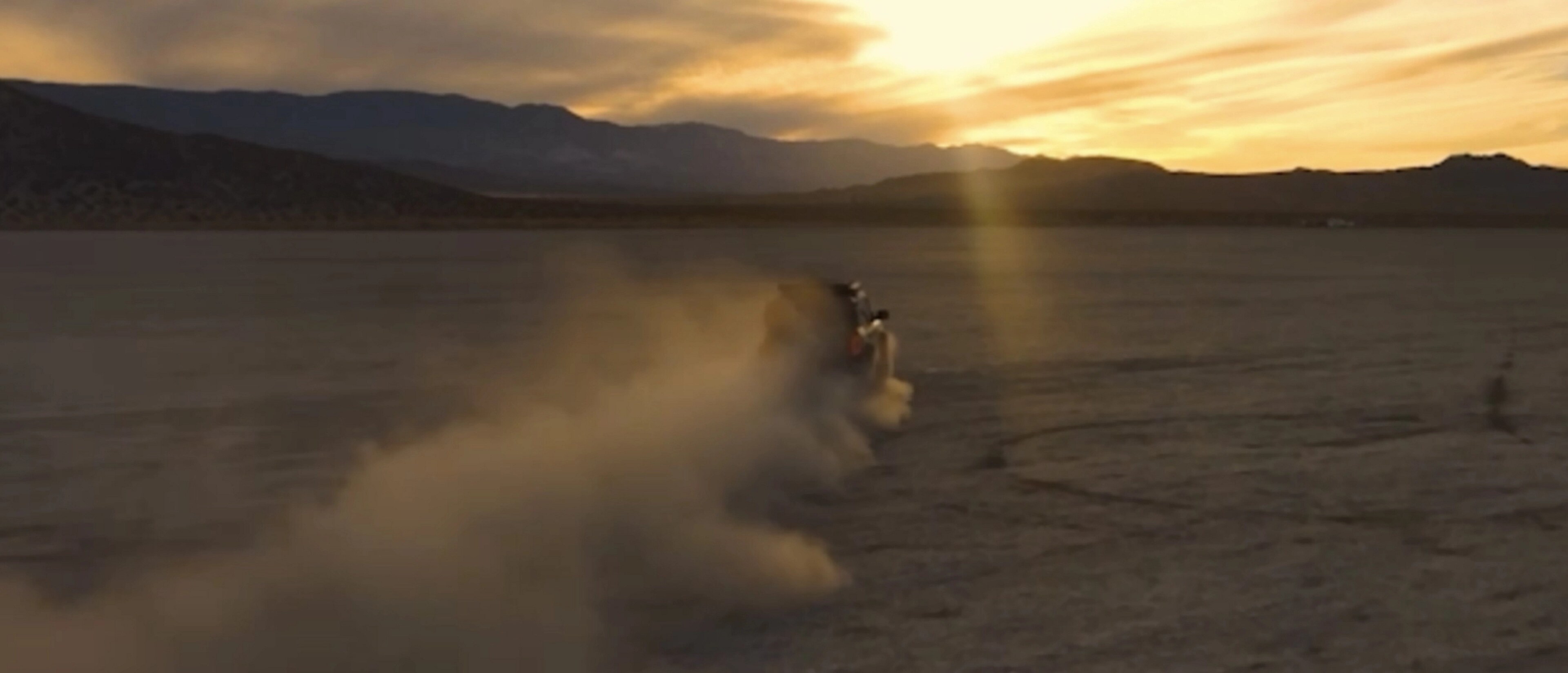 Un VUS Ford Bronco® 2026 roulant dans un désert poussiéreux devant un coucher du soleil.