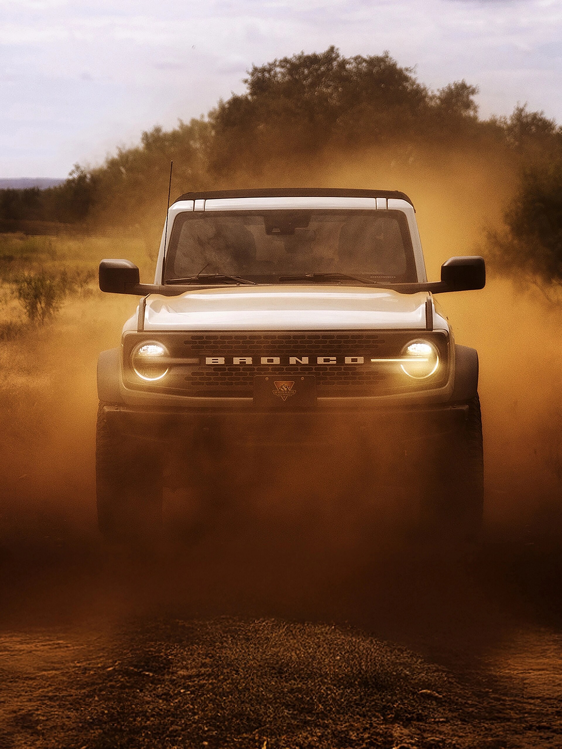 L’avant d’un VUS Ford Bronco® 2026, ses phares brillant à travers un nuage de poussière rouge.