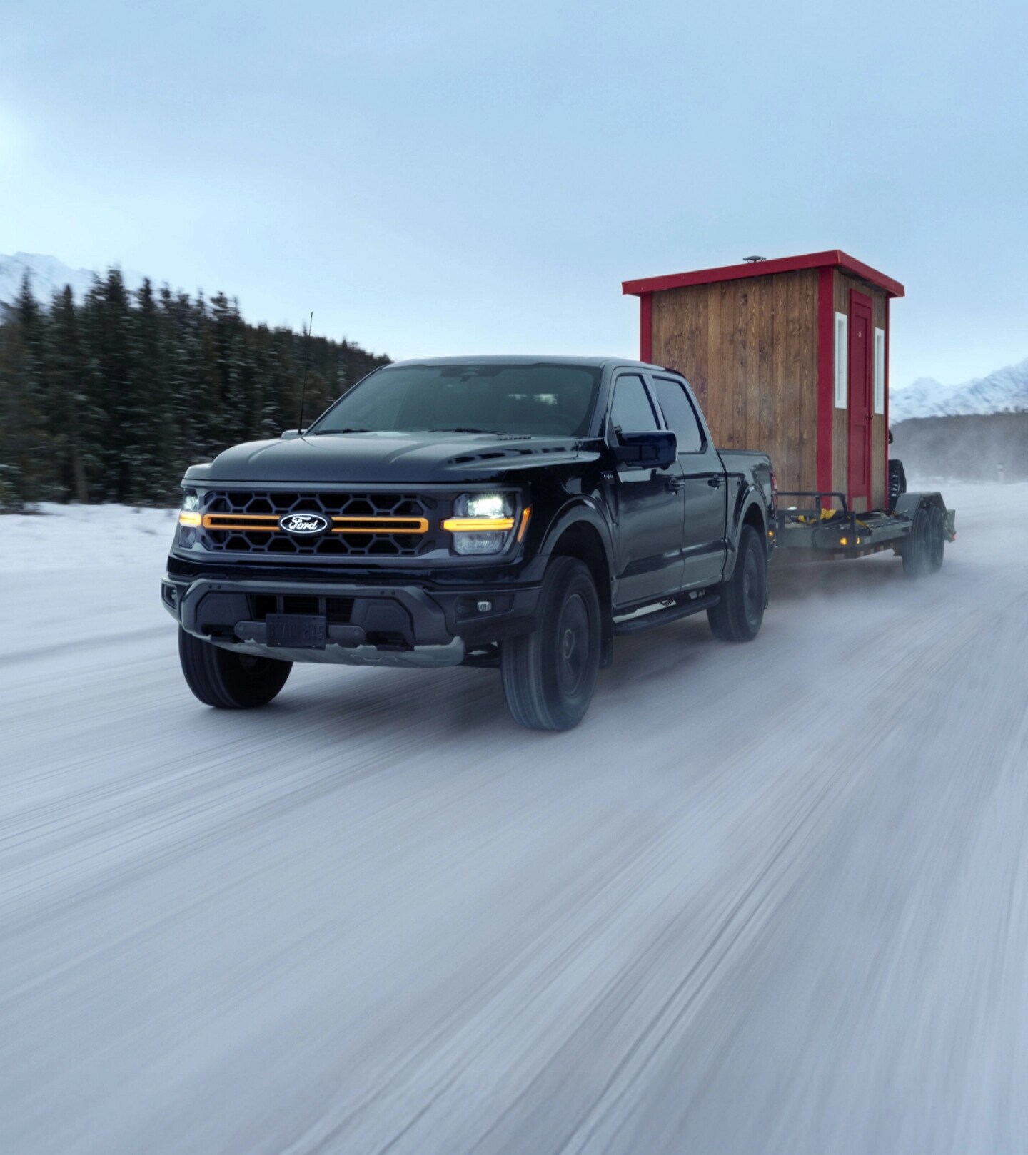 Un F-150 Tremor remorquant un abri de pêche sur glace et un VTT sur une route de montagne gelée.