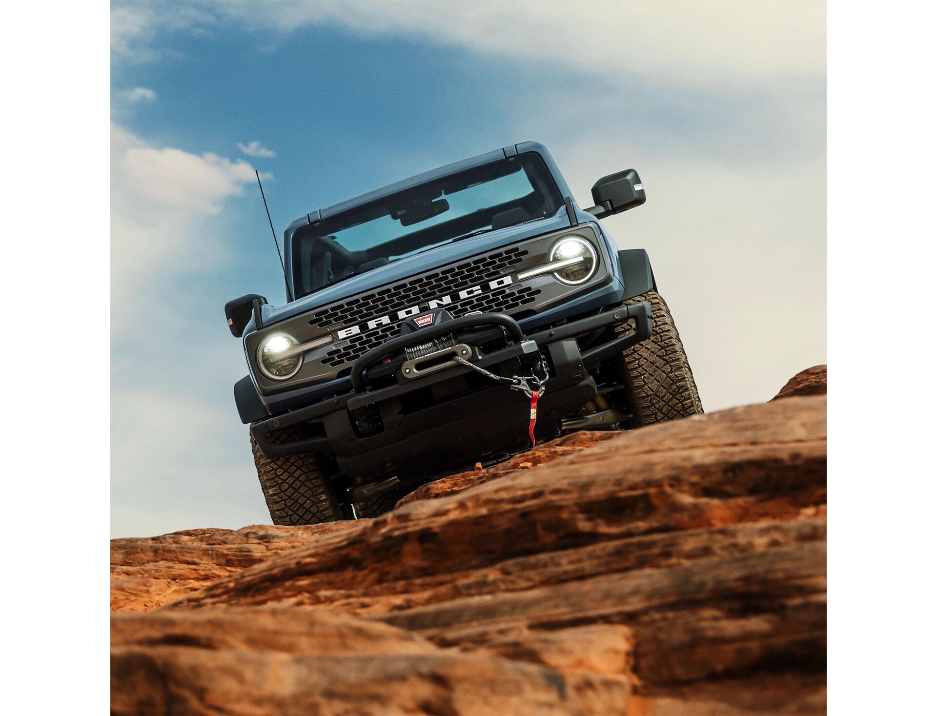 Vue de face d'un Ford Bronco gris-bleu garé au sommet d'un terrain rocheux. 