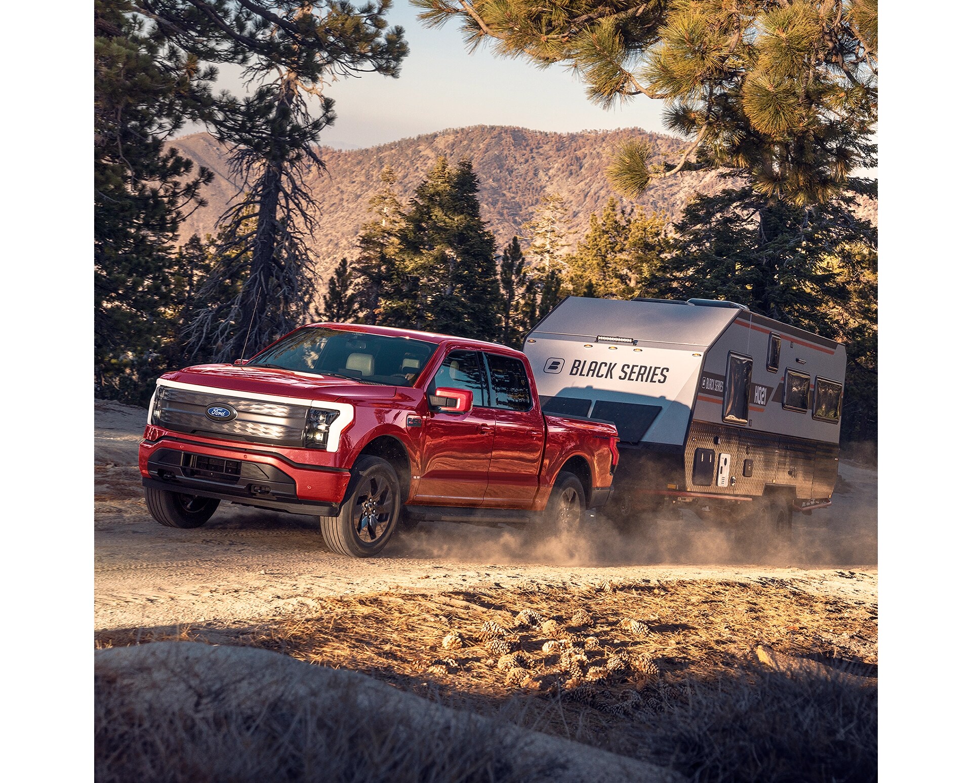 Vue de profil trois quarts d'un F-150 Lightning rouge remorquant une caravane sur un sentier forestier dans un décor montagneux.