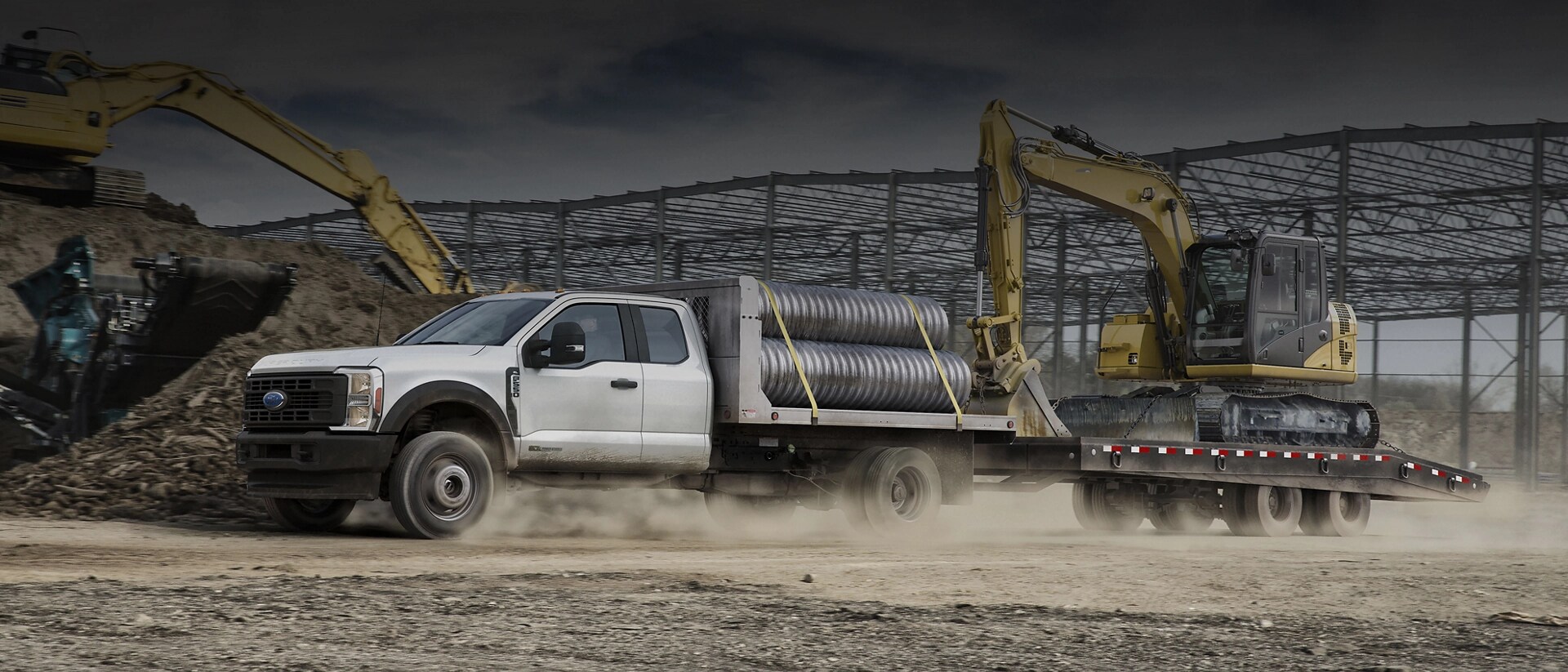 Un Ford Super Duty® à châssis-cabine 2026 chargé de tuyaux et tirant une remorque avec une rétrocaveuse
