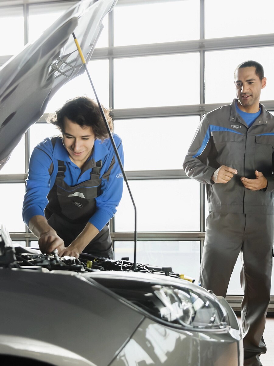 Une personne travaille sur un véhicule pendant que deux autres individus l’observent