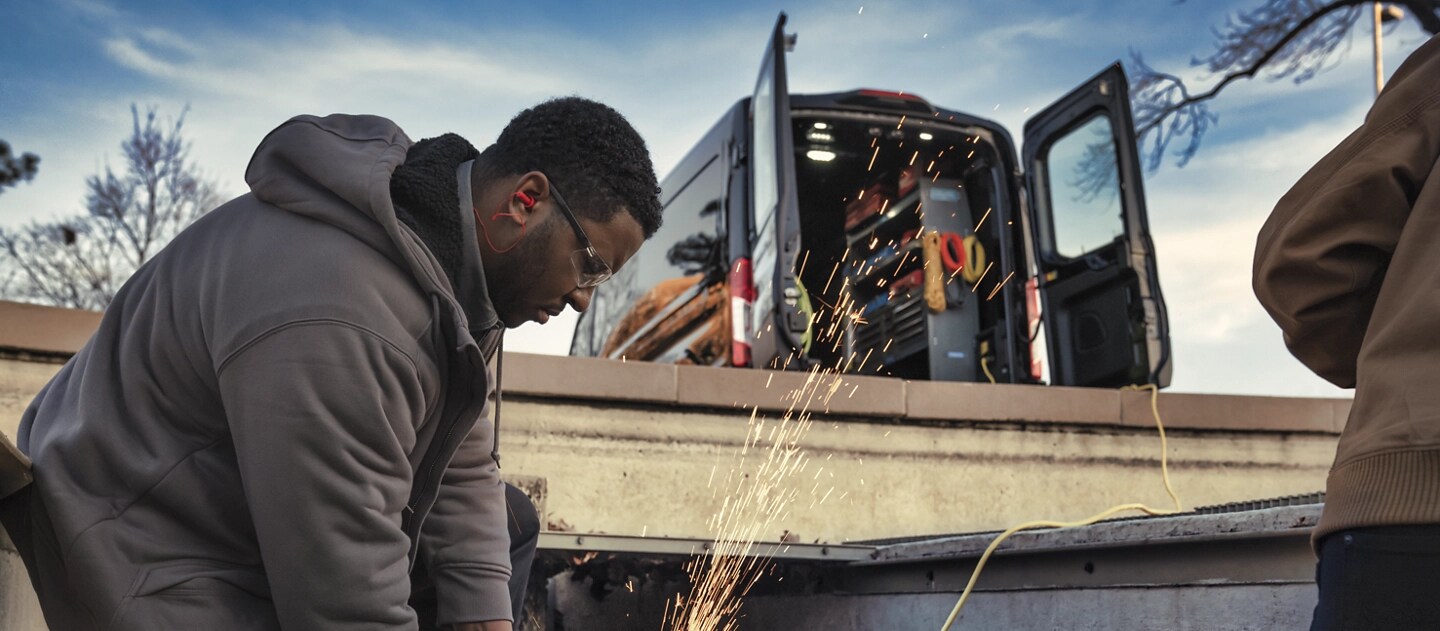 Une fourgonnette Ford E-Transit™ 2025 avec les portières arrière ouvertes alors qu’un travailleur se branche dans Pro Power Onboard™