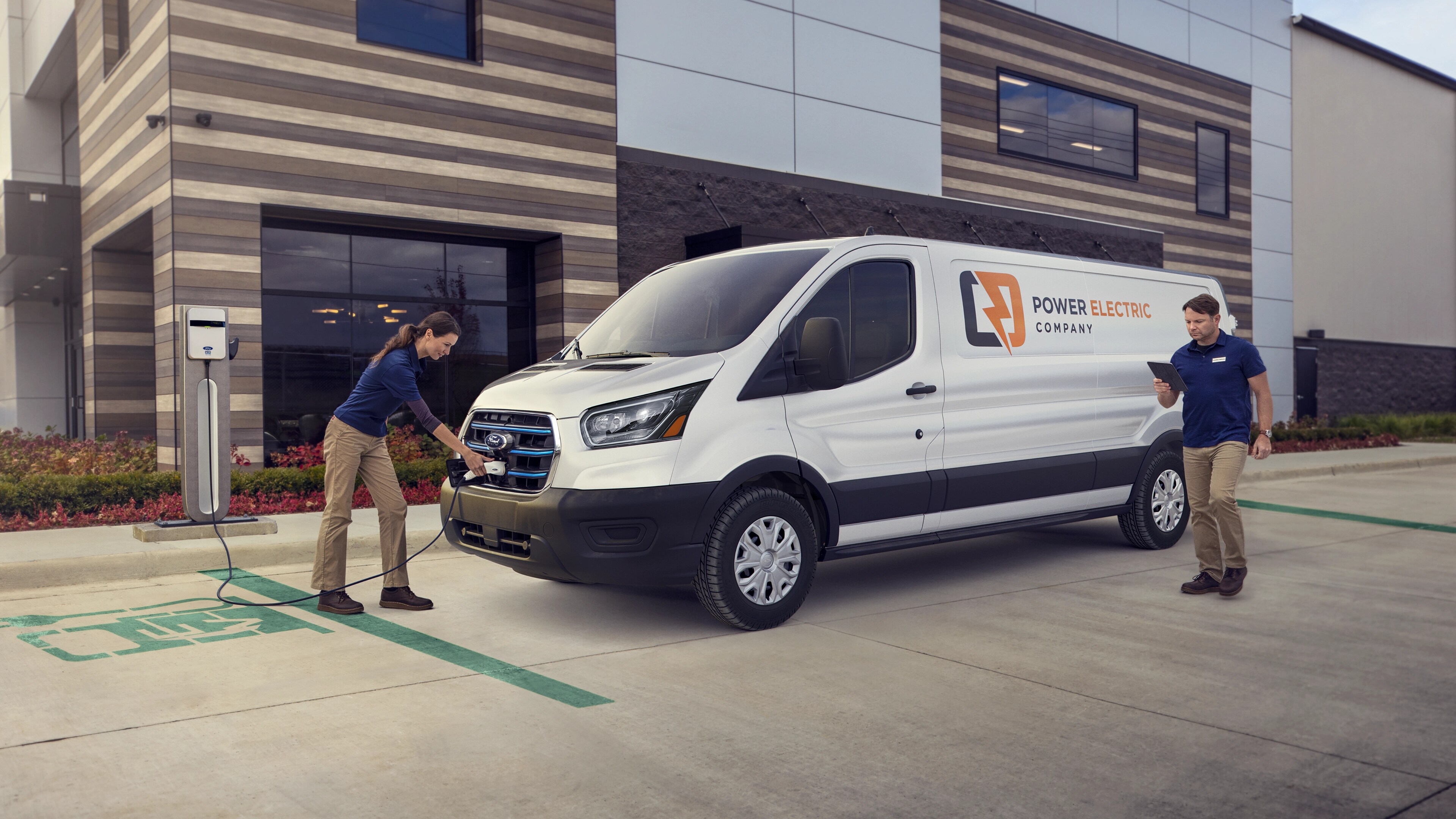 Une fourgonnette Ford E-Transit™ 2025 blanche stationnée et chargée par deux travailleurs à l’extérieur d’une entreprise