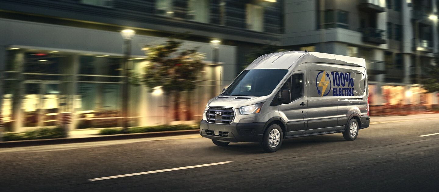 Une fourgonnette Ford E-Transit™ 2025 grise circulant dans une rue de la ville