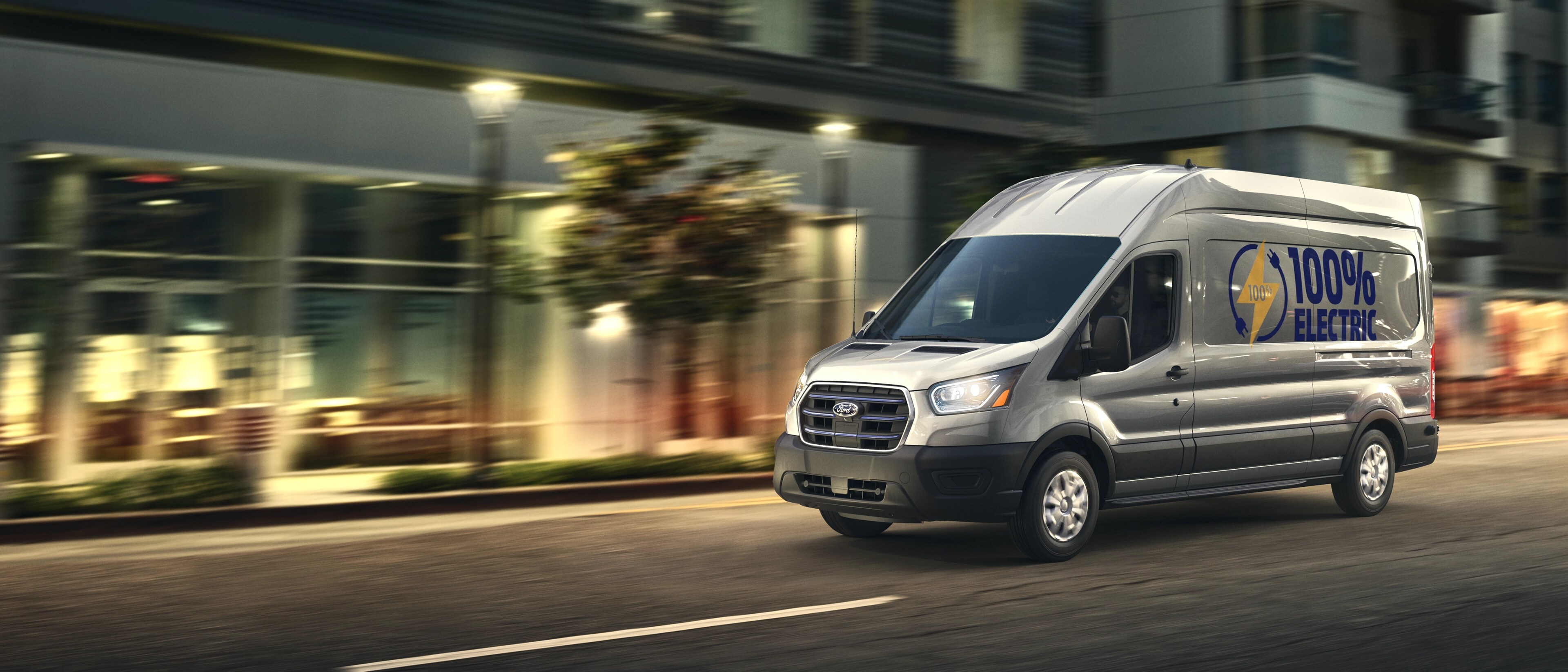 Une fourgonnette Ford E-Transit™ 2025 grise circulant dans une rue de la ville