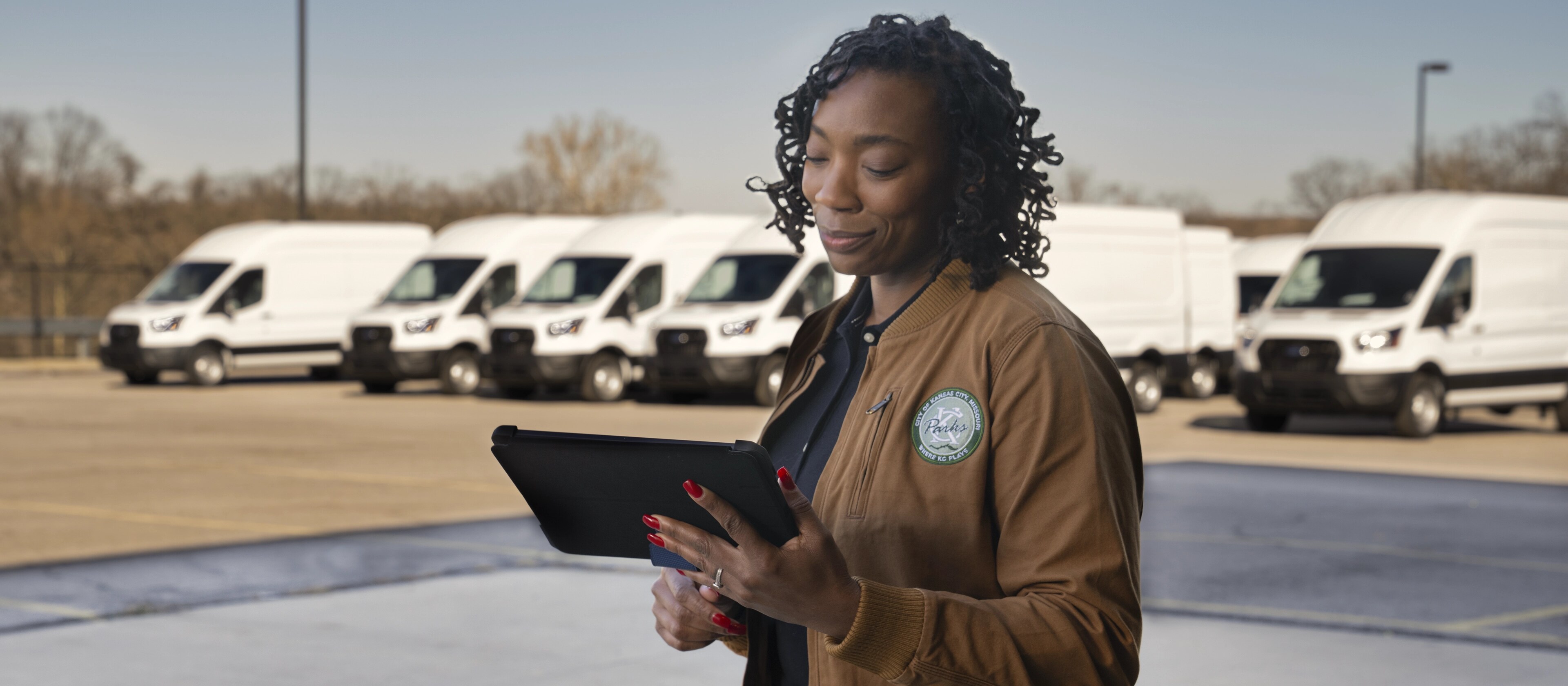 Un parc automobile de véhicules Ford E-Transit™ 2025 blancs stationnés derrière un travailleur tenant une tablette