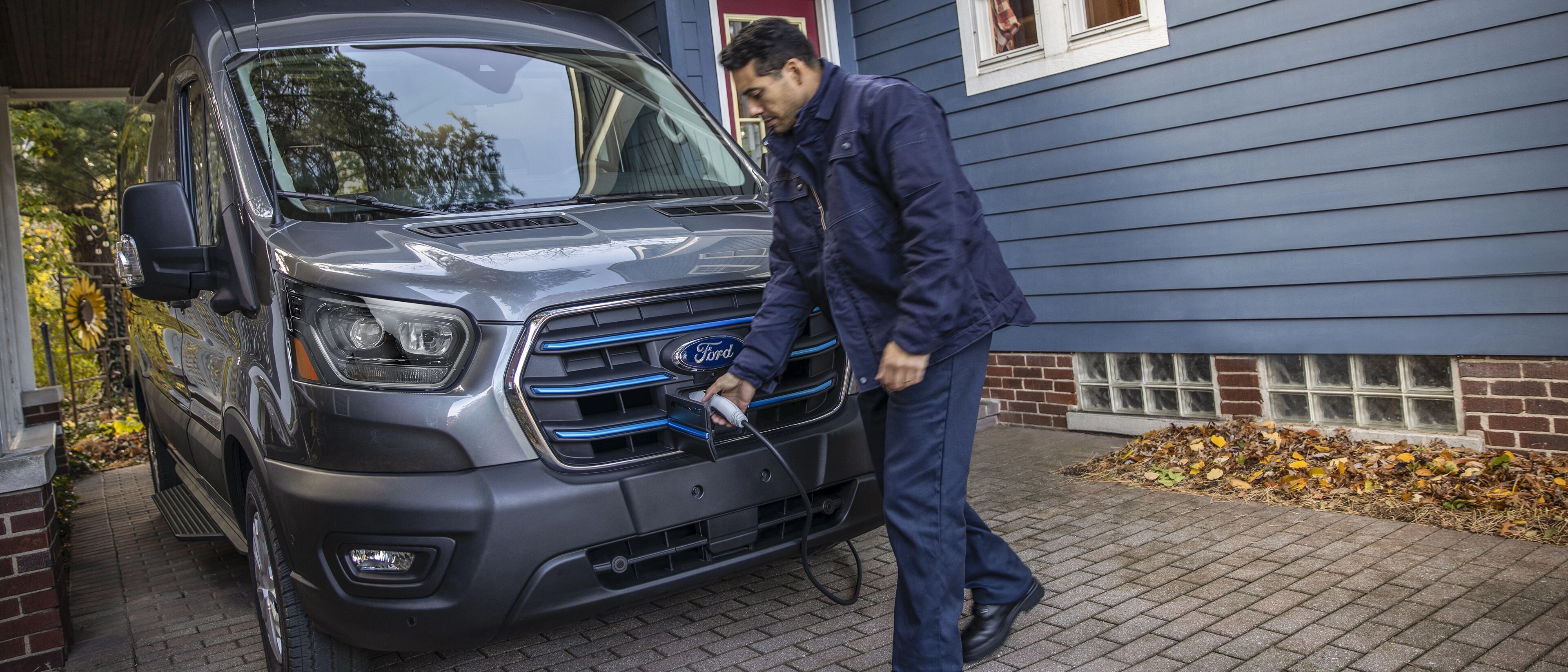 Une fourgonnette Ford E-Transit™ 2025 grise stationnée dans une entrée de maison chargée pour la nuit