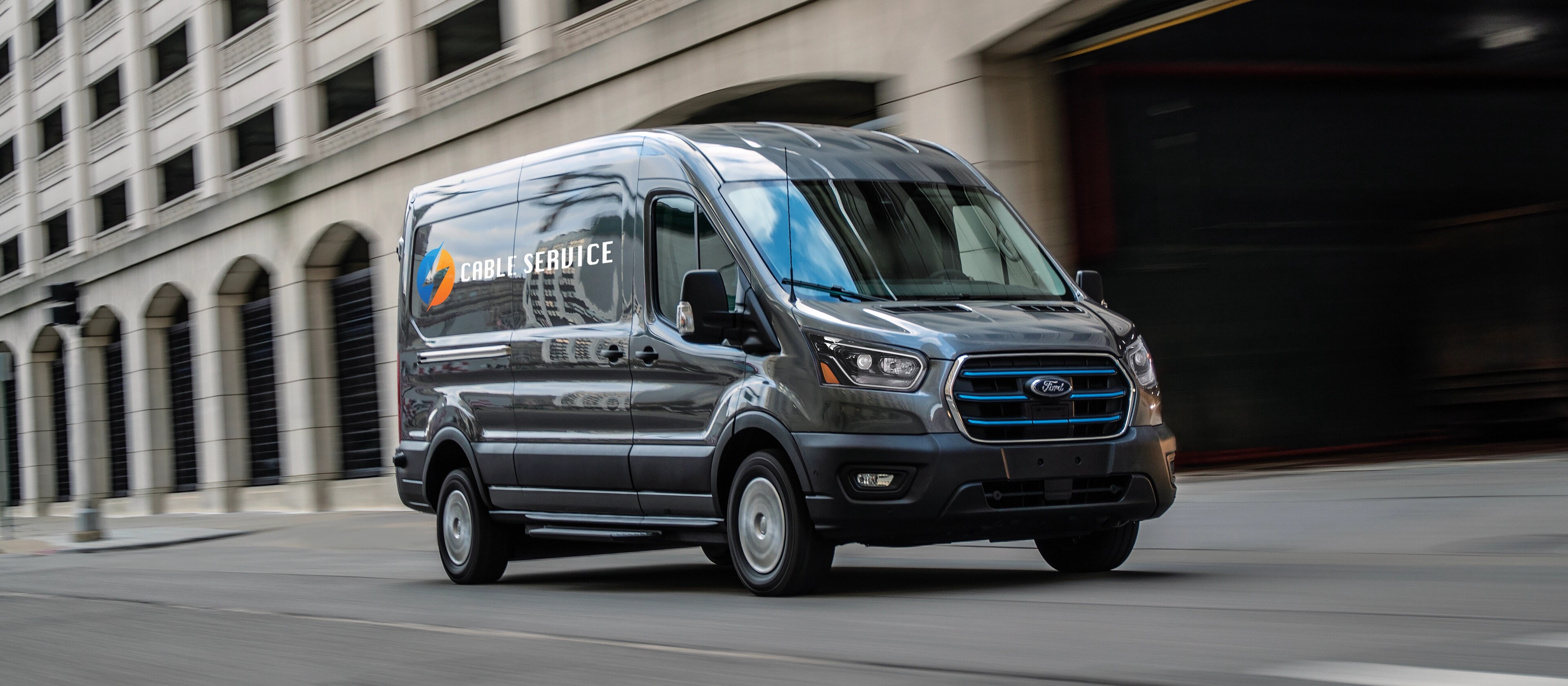 Une fourgonnette Ford E-Transit™ 2025 bleue circulant dans une rue de la ville