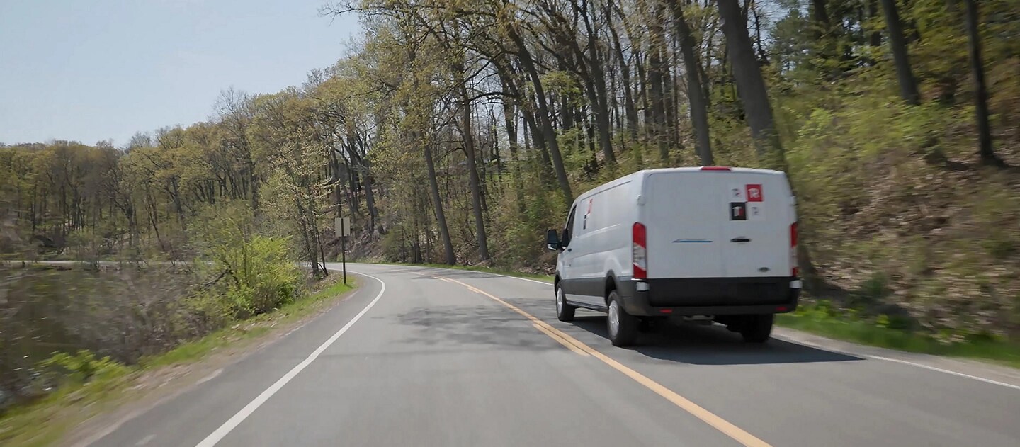 Une fourgonnette Ford E-Transit™ 2025 blanche circulant sur un terrain boisé