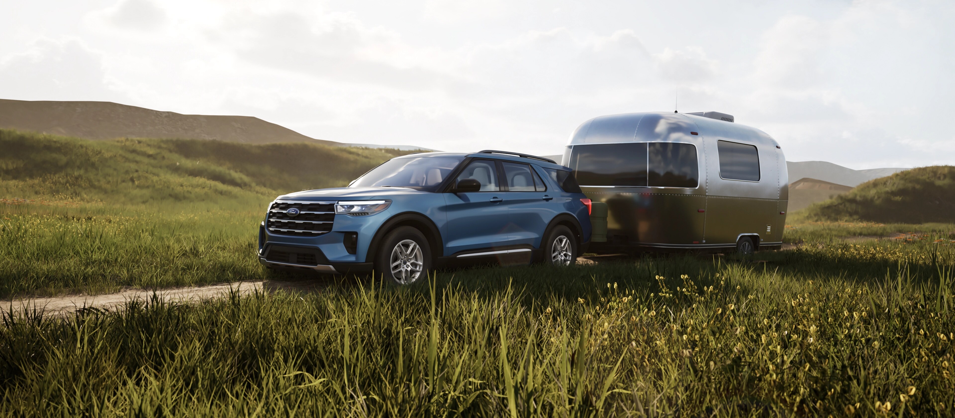 Un VUS Ford Explorer® 2025 tirant une remorque de voyage sur une route de terre à travers une prairie