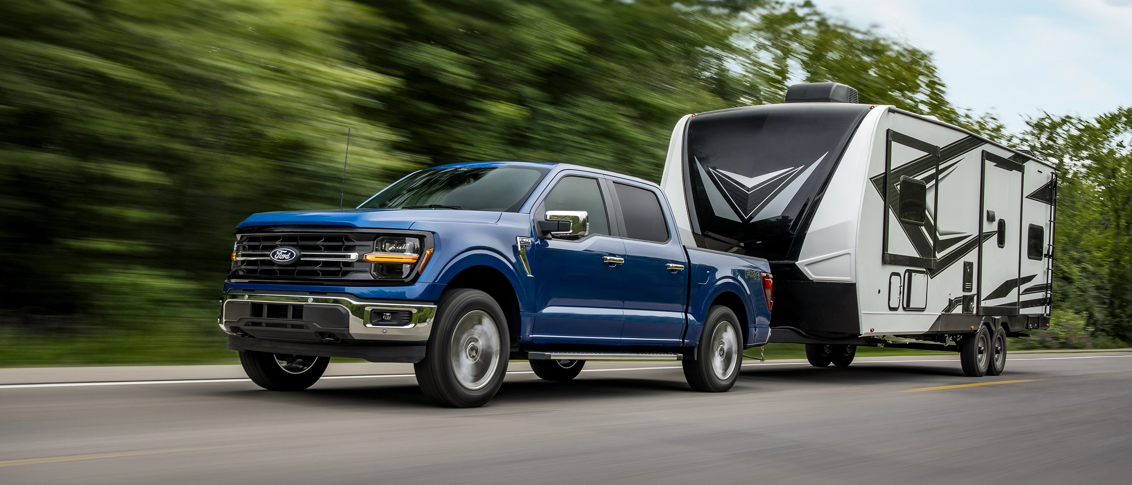 Camion Ford F-150® 2025 fixé à une remorque de camping circulant dans une zone boisée