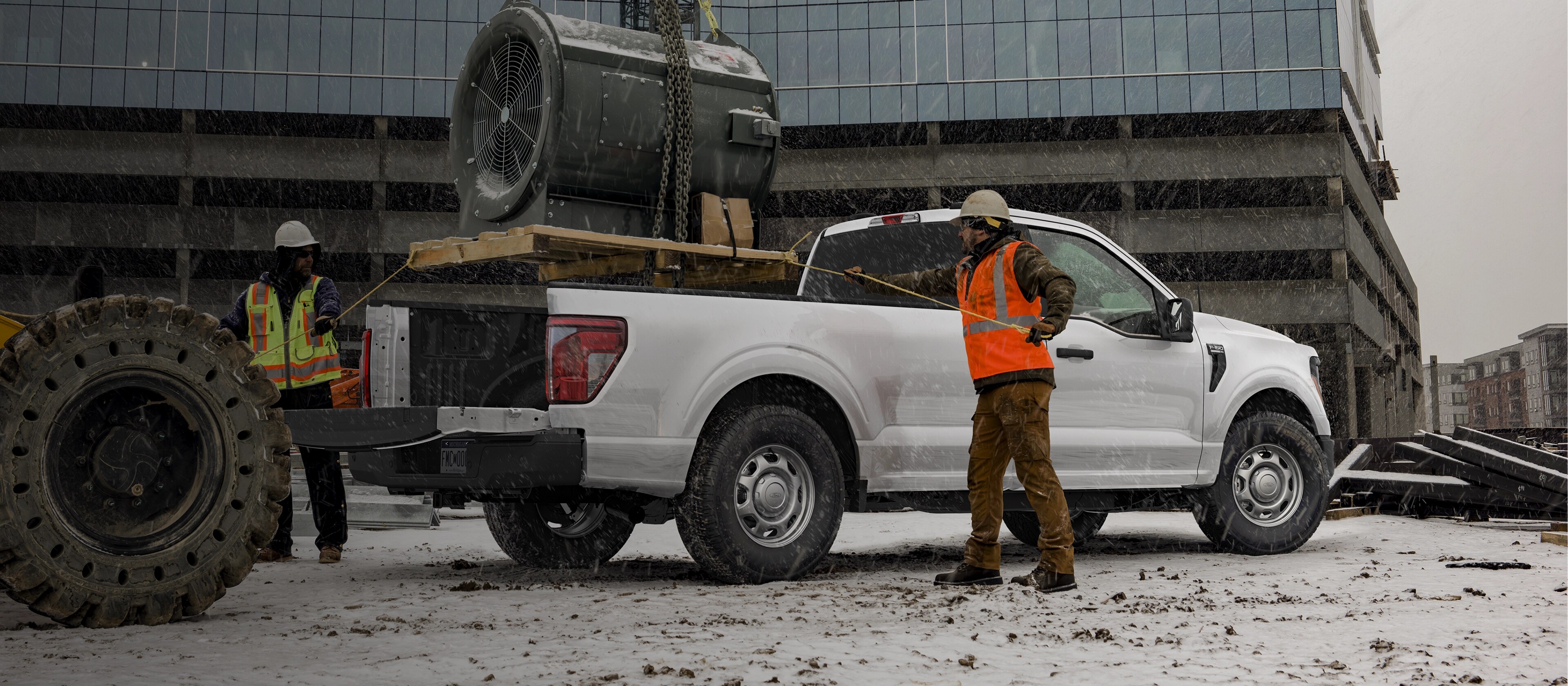 Deux travailleurs de la construction attachent une cargaison dans la caisse d’une camionnette Ford F-150® 2025 stationnée sur un chantier