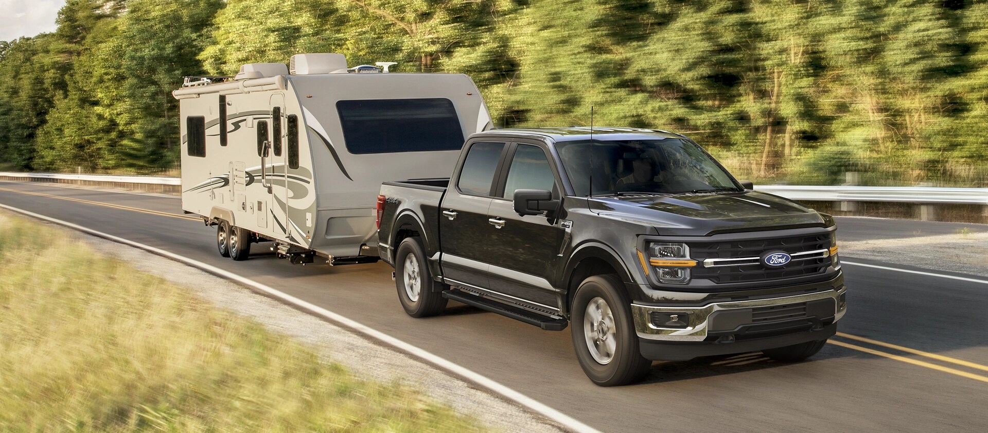 Camion Ford F-150® XLT 2025 tirant une remorque de camping sur une route bordée d’arbres