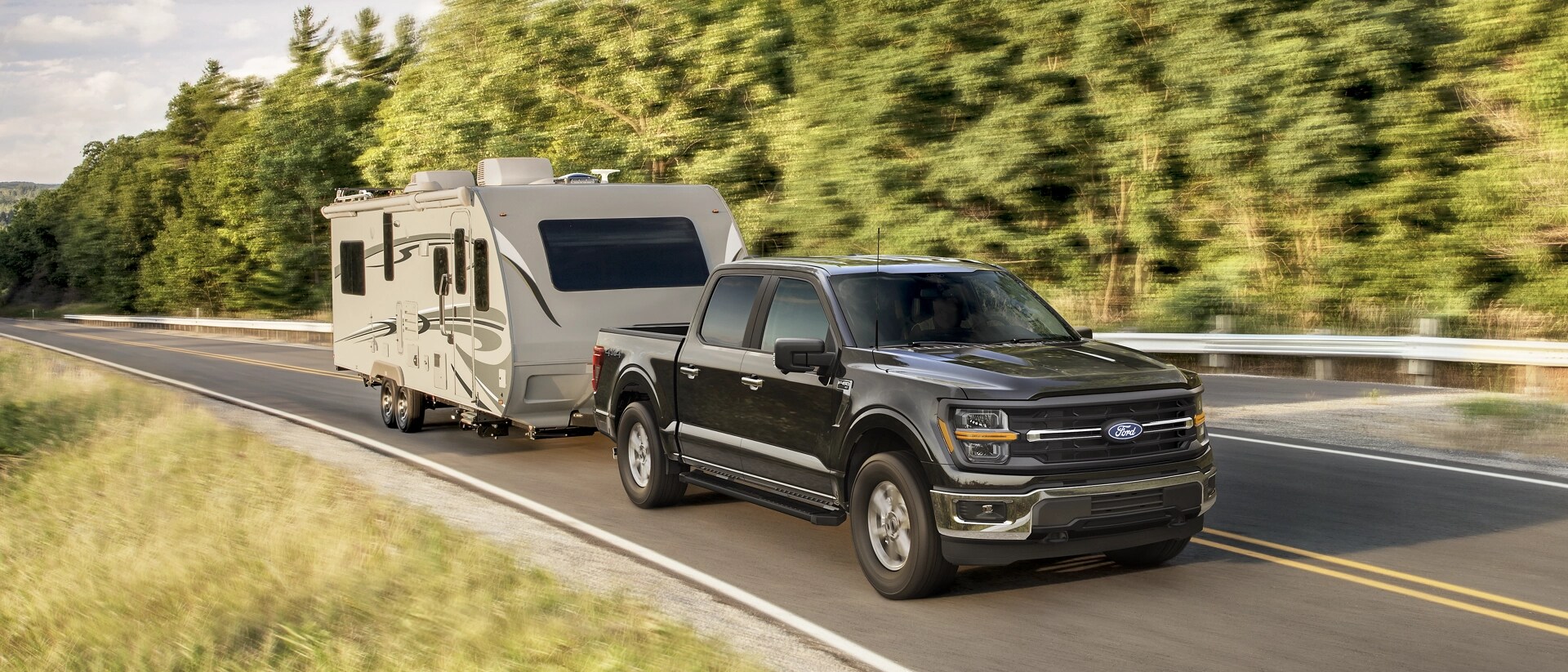 Modèle Ford F-150® XLT 2025 en bronze foncé métallisé tirant une caravane sur une route bordée d’arbres