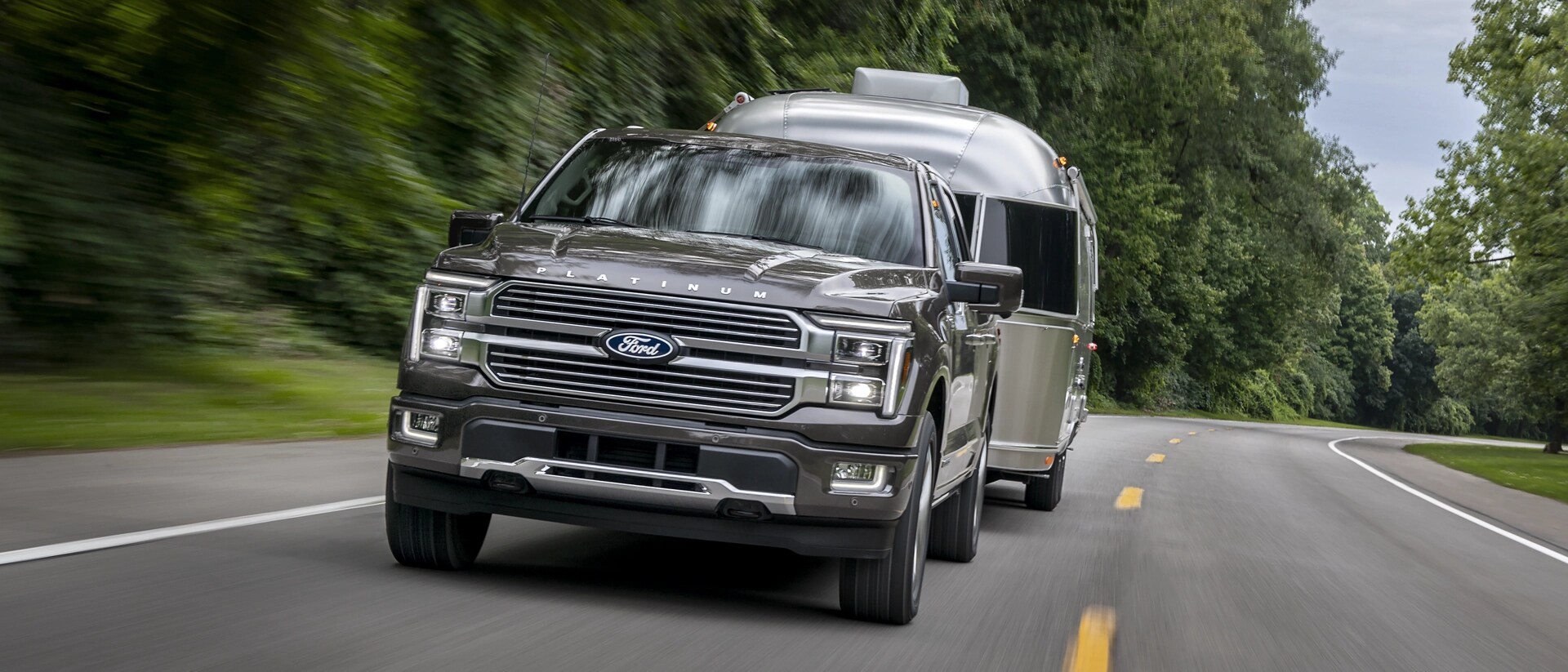 Camion Ford F-150® Platinum® 2025 tirant une remorque de camping sur une route bordée d’arbres