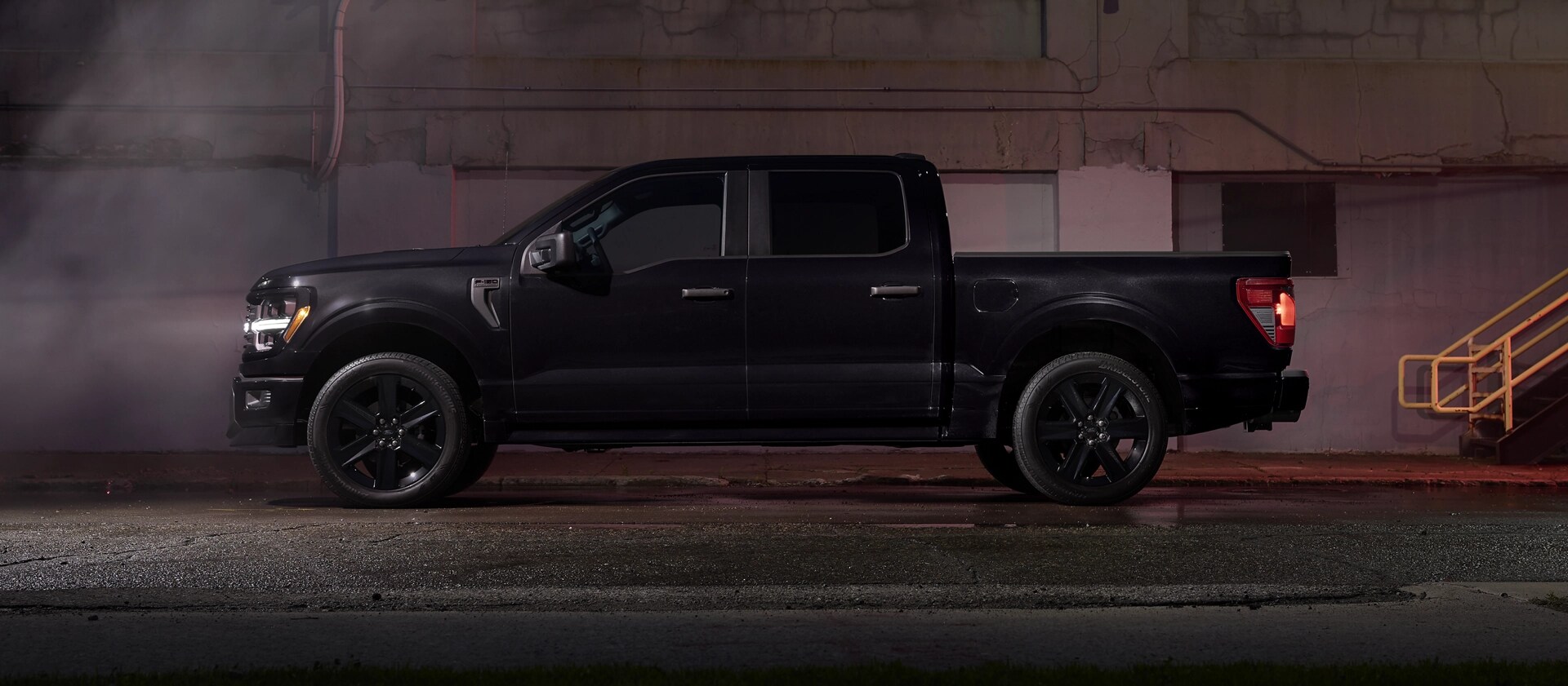 Un Ford F-150® STX 2025 noir avec l’ensemble Lobo™ stationné près d’un bâtiment urbain la nuit