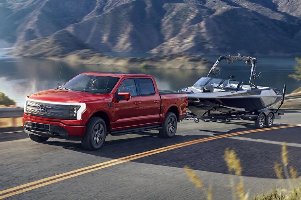 Un Ford F-150® Lightning® 2025 transportant un bateau sur une remorque sur une autoroute près d’un lac de montagne