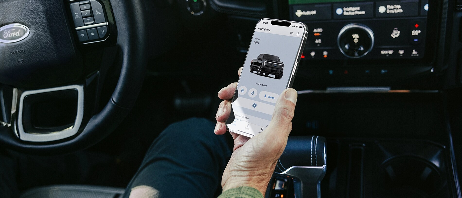 La main d'un conducteur assis dans un camion Ford F-150® Lightning® 2025, tenant un téléphone intelligent avec l'application FordPass®.