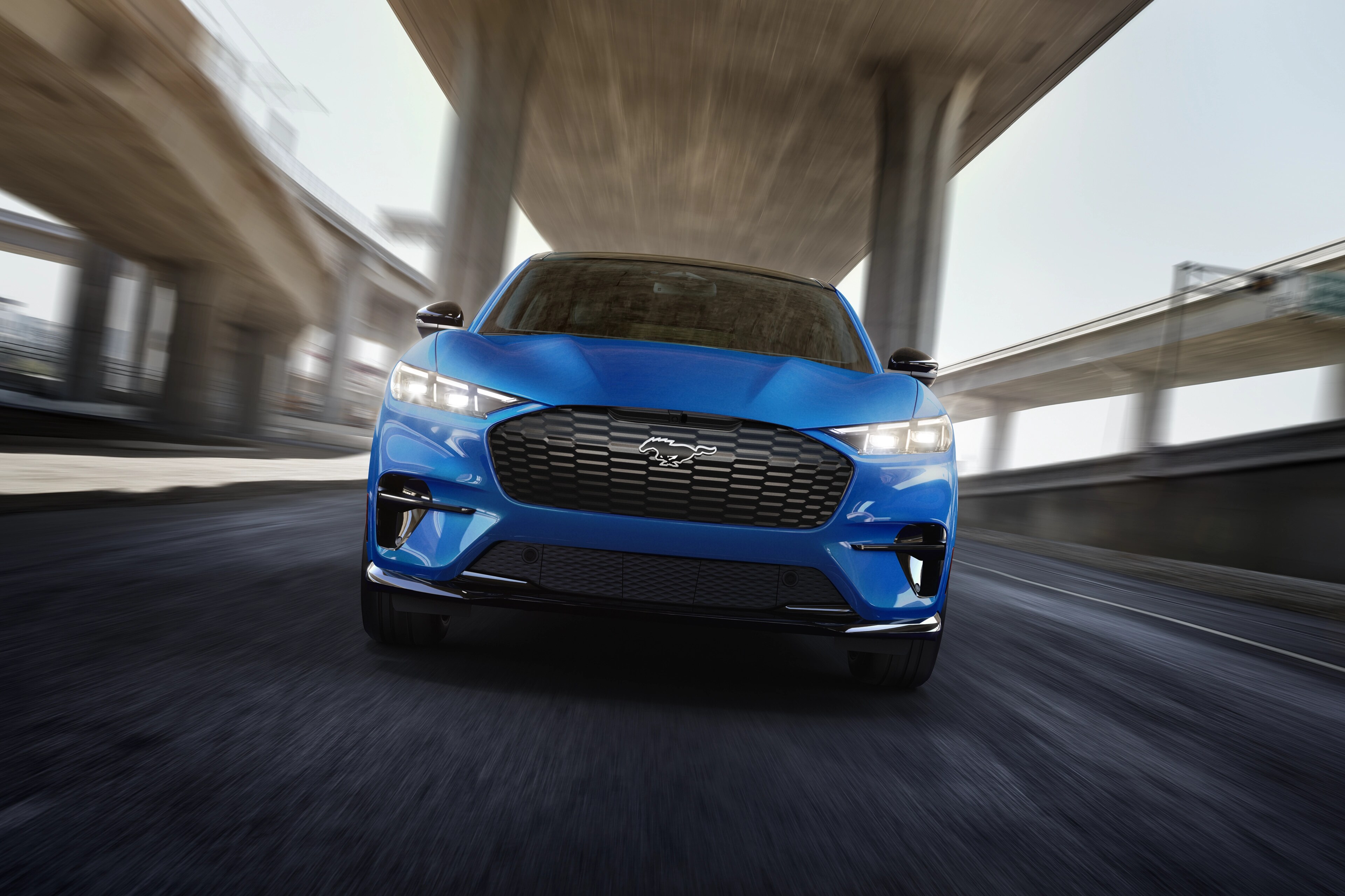 Vue avant d’un modèle Mustang Mach-E® GT 2025 conduit sur une autoroute avec un arrière-plan flou