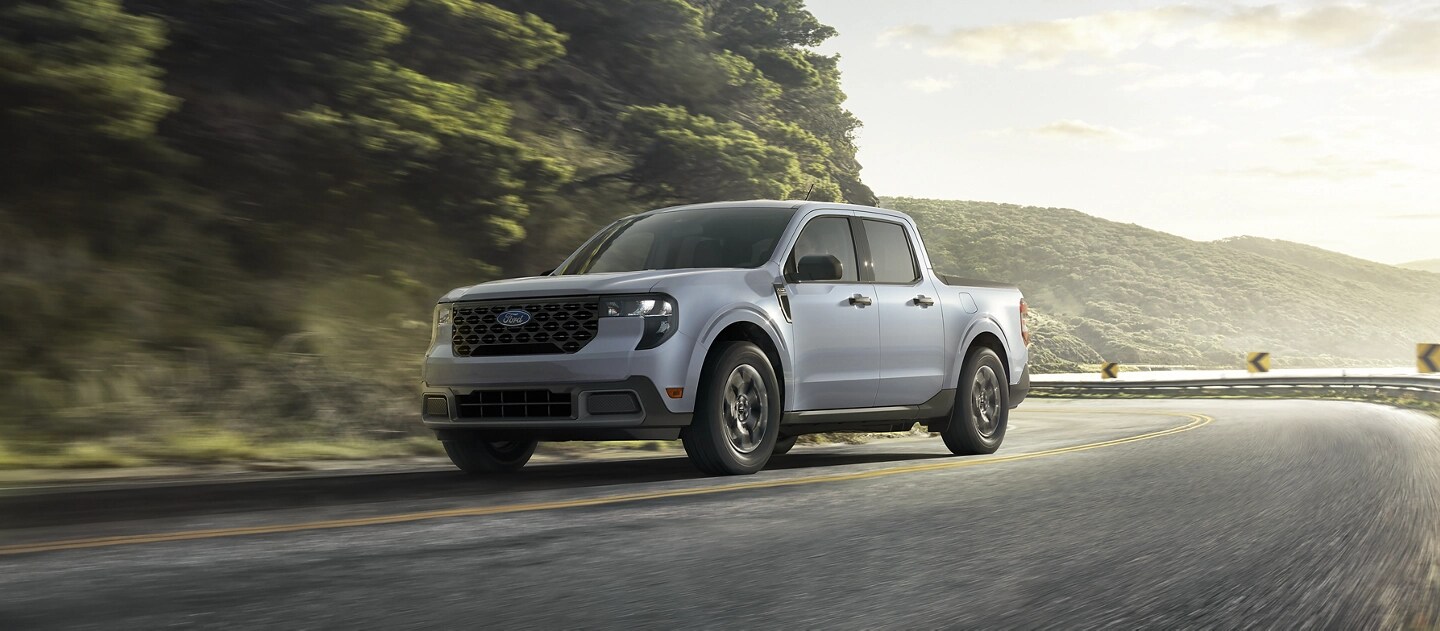 Un Ford Maverick® 2025 circulant sur une route sinueuse près d’un lac de montagne