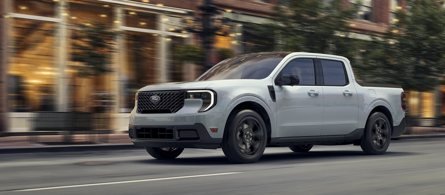Une camionnette Ford Maverick® 2025 avec ensemble décor noir circulant dans une rue de la ville le soir