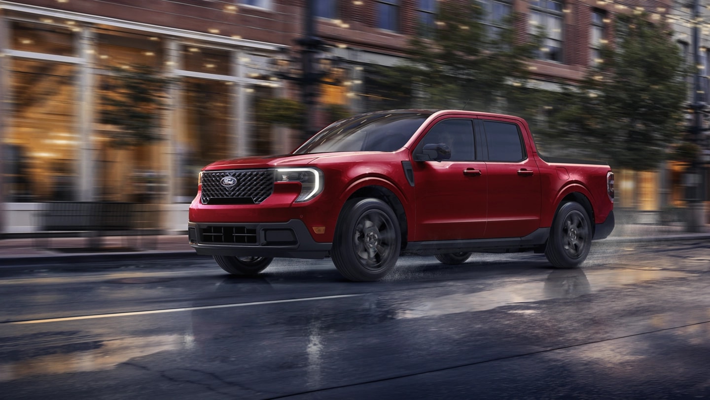 Un camion Ford Maverick® 2025 rouge circulant dans une rue de ville pluvieuse